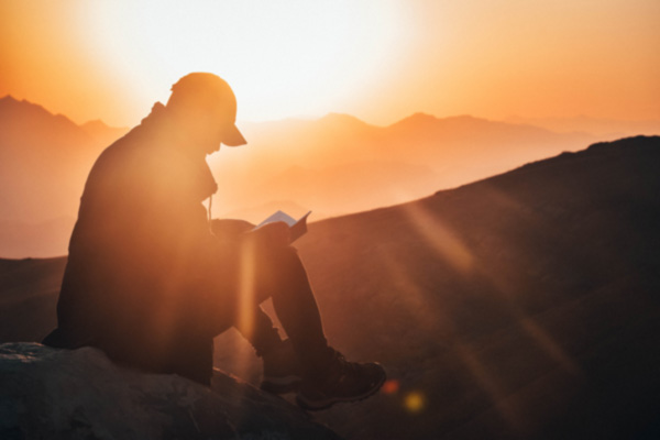 Silhouette of man relaxing on mountain with book not facing addiction