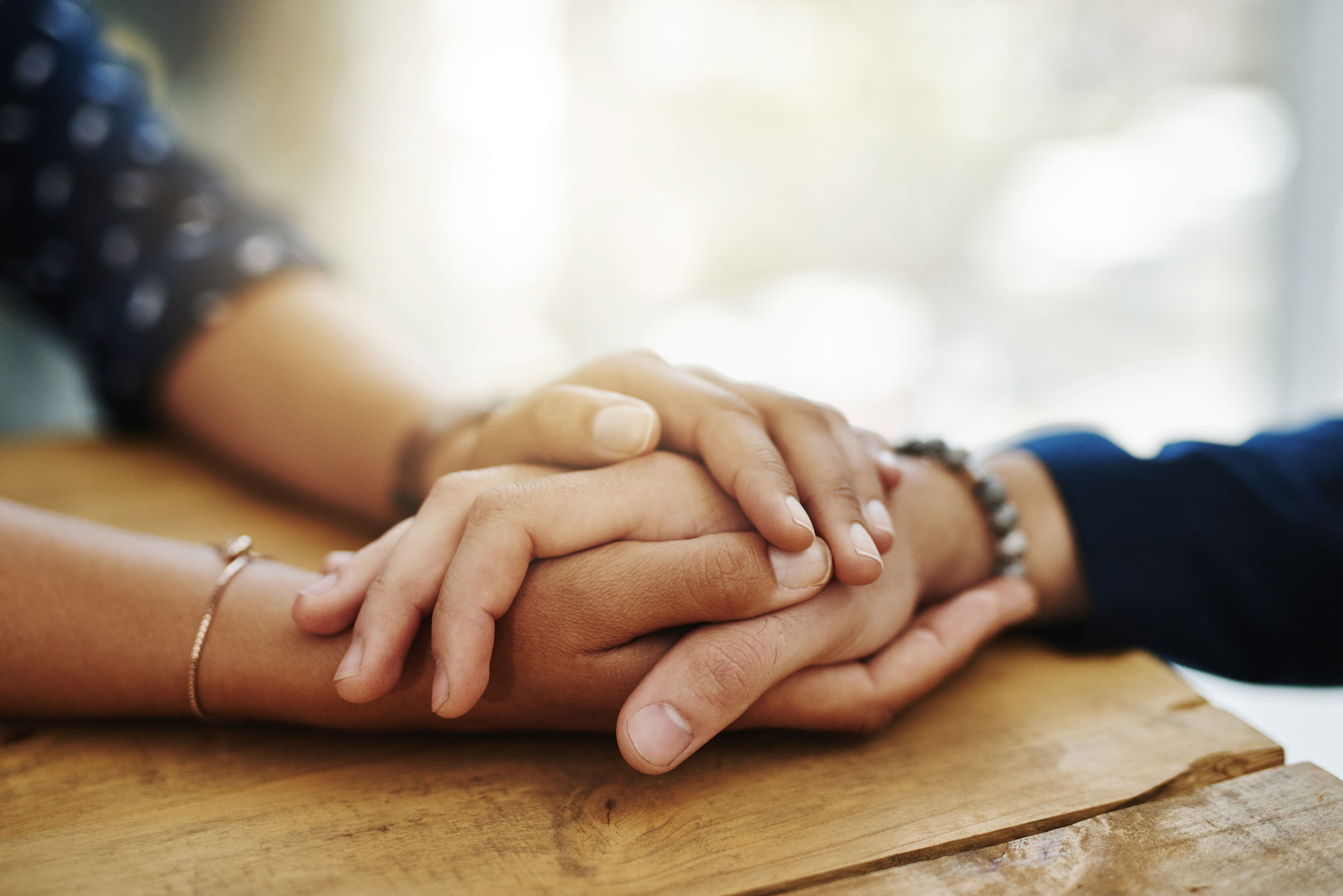 two people clasping hands to provide support to one another across a table, representative of trauma informed care