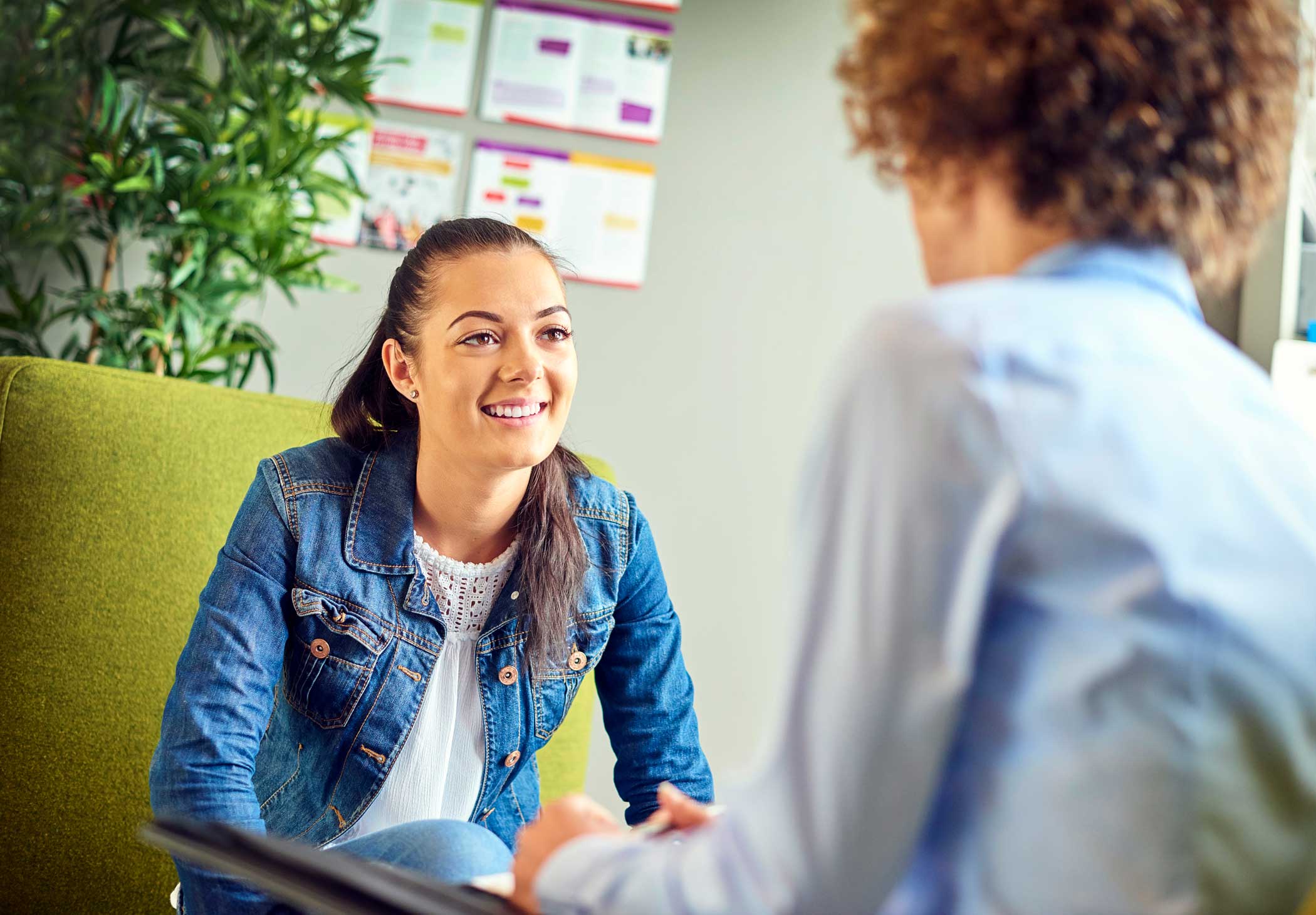 woman in denim jacket sitting with her counselor in a well lit office engaging in mental health counseling
