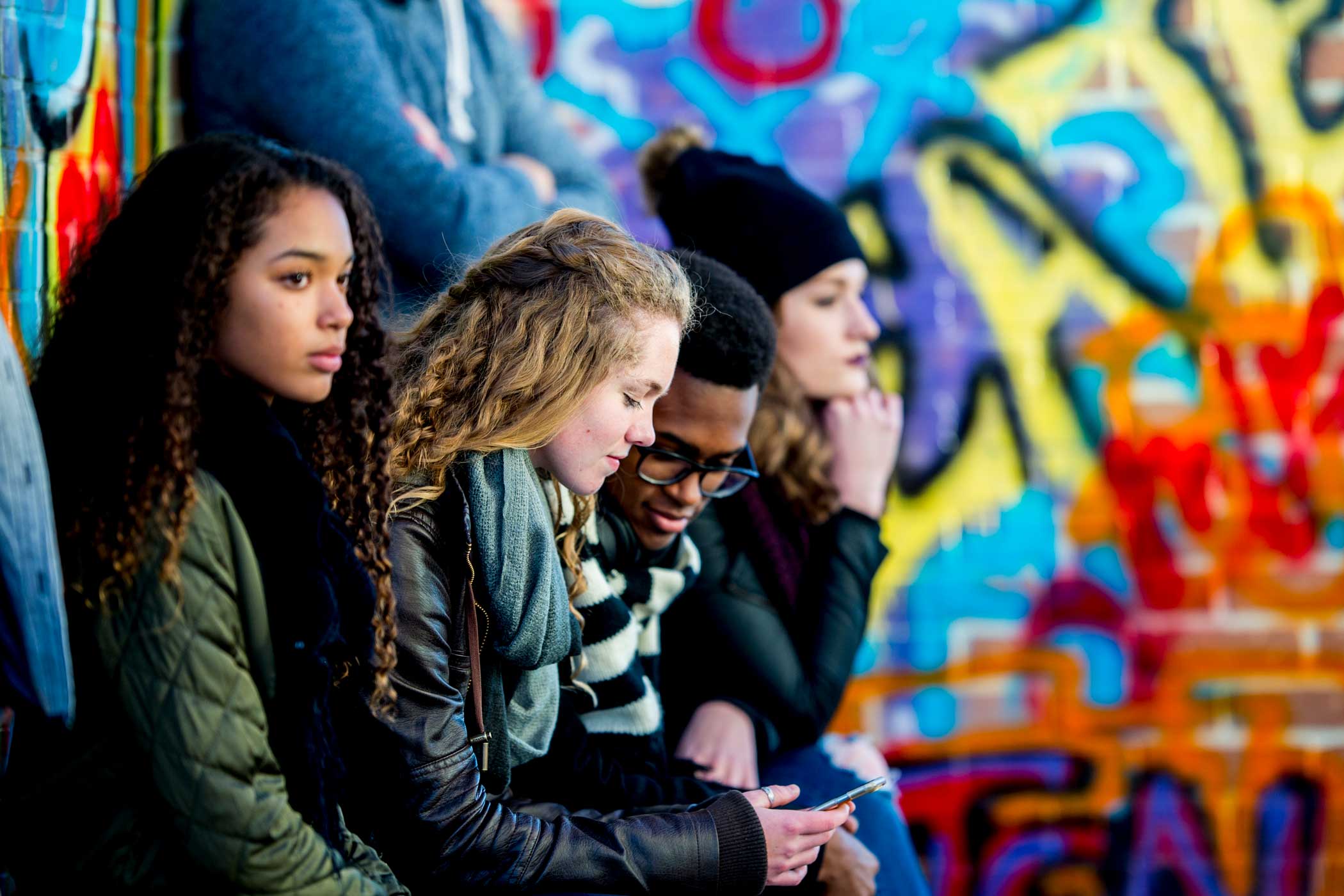 a group of youth sitting next to a colorfully painted wall.