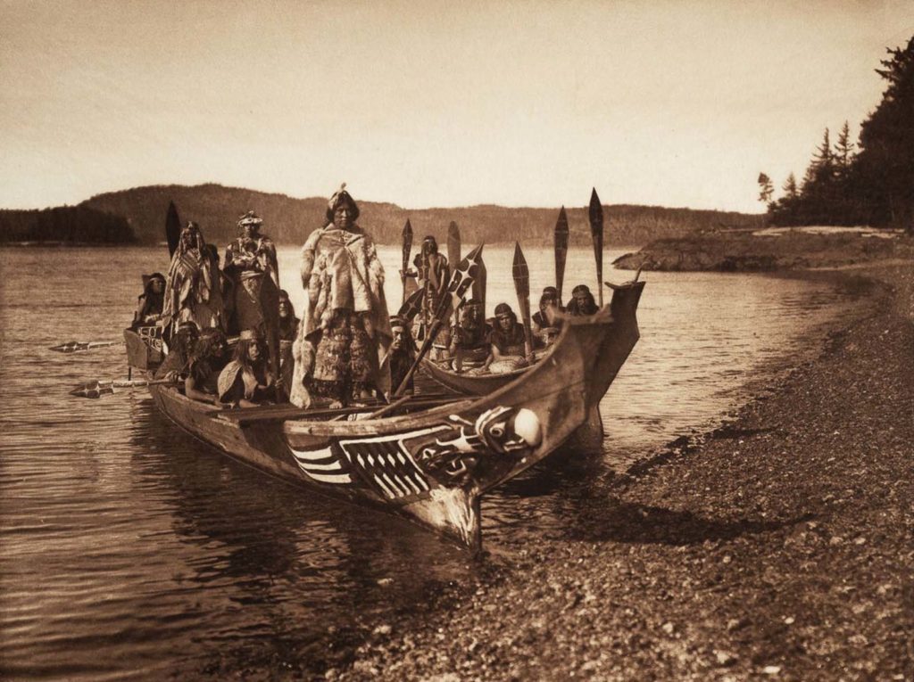 A picture of several Native Americans in a canoe arriving at the shore for a Kwakiutl wedding.