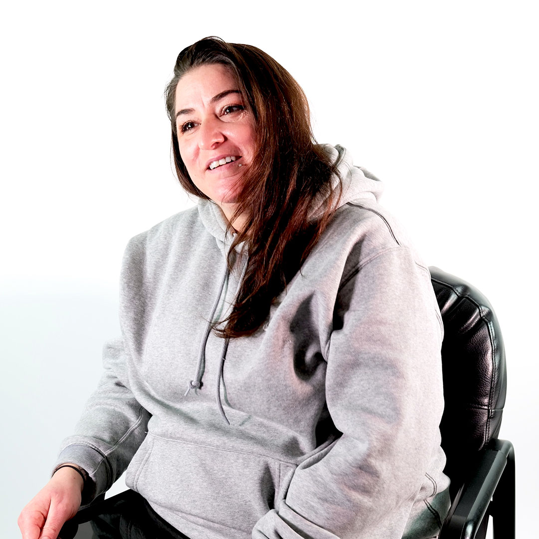 Sandra seated in interview chair before white background wearing a gray hoodie
