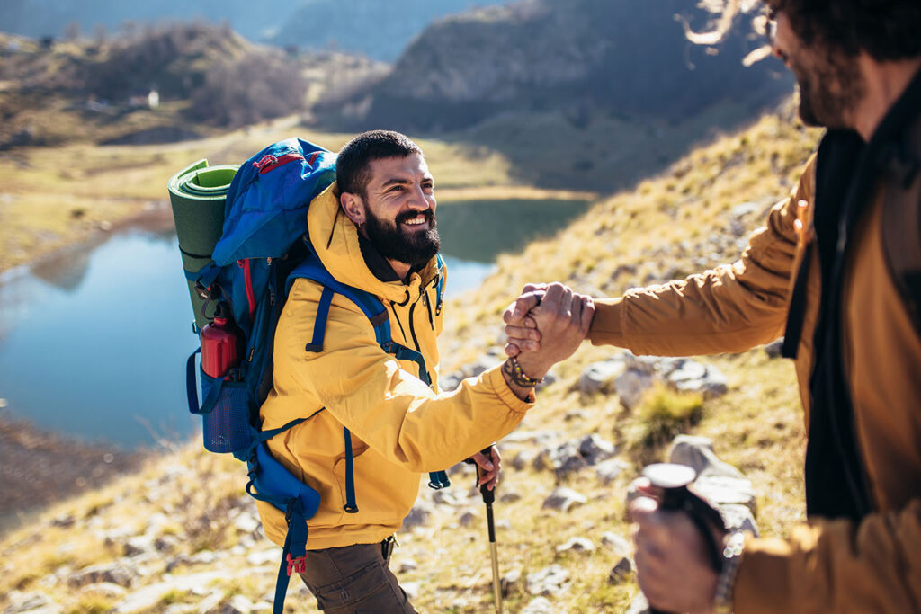 A smiling hiker receives a helping hand up a hillside from a friend.