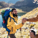 A smiling hiker gets a helping hand from their friend.