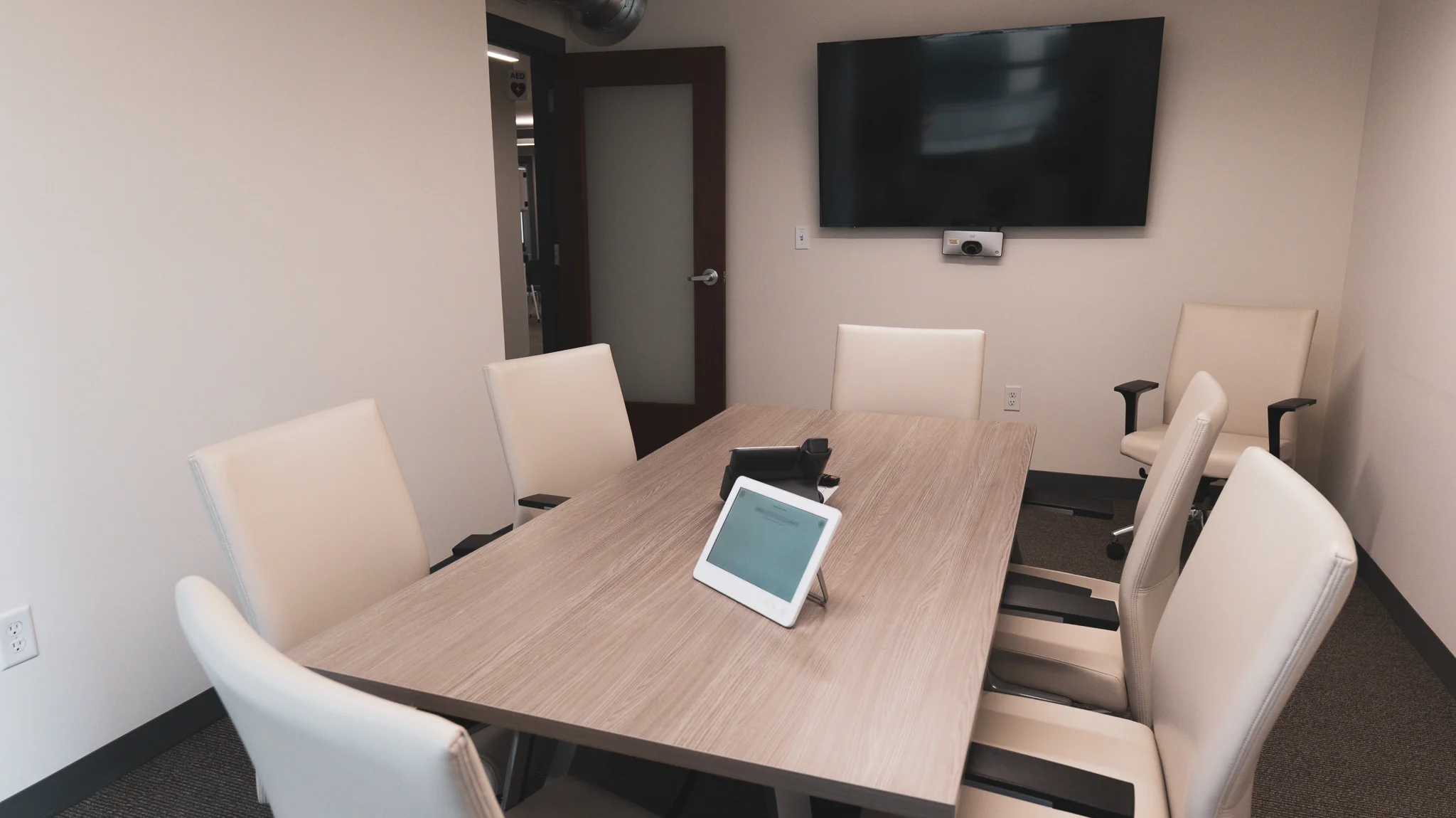 ths-olive-branch-location_board-room THS Olive Branch conference room with light wood table, cream leather chairs, wall-mounted display screen, and video conferencing equipment