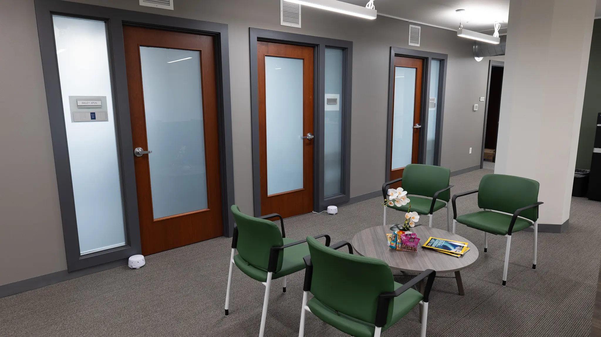 ths-olive-branch-location_lobby THS Olive Branch waiting area with green upholstered chairs, round coffee table, and frosted glass office doors along a modern hallway