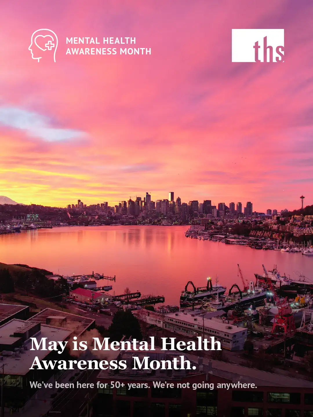 A Mental Health Awareness Month launch graphic for Therapeutic Health Services. In the top left, a white Mental Health Awareness Month icon. The THS logo appears in the top right on a white background. A stunning aerial photograph of the Seattle skyline at sunrise fills the frame, with the city reflected in Lake Union below and a dramatic pink, orange, and purple sky above. The Space Needle is visible on the right side of the skyline. Bold white text at the bottom reads: "May is Mental Health Awareness Month." Below in smaller white text: "We've been here for 50+ years. We're not going anywhere."