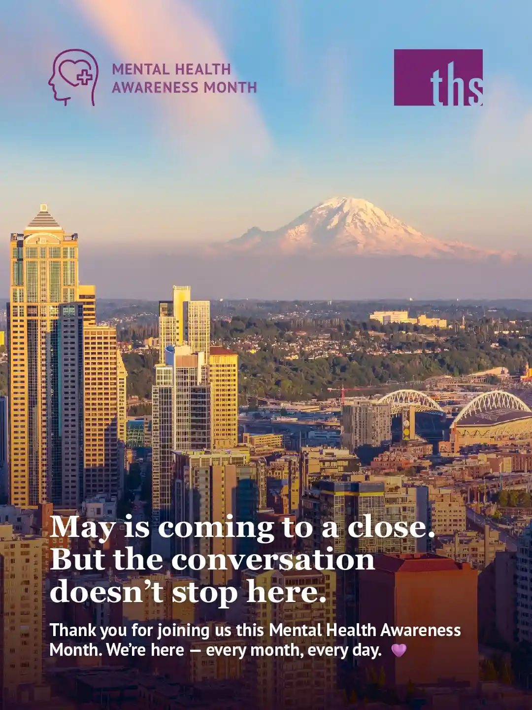 A Mental Health Month wrap-up graphic for Therapeutic Health Services. In the top left, a purple Mental Health Awareness Month icon. The THS logo appears in the top right. An aerial photograph of the Seattle skyline at golden hour fills the frame, with Mt. Rainier's snow-capped peak rising prominently in the background under a soft pink and blue sky. The city's buildings glow warmly in the evening light, with Lumen Field visible on the right. A subtle dark gradient fades up from the bottom of the image. Bold white text reads: "May is coming to a close. But the conversation doesn't stop here." Below in smaller white text: "Thank you for joining us this Mental Health Awareness Month. We're here — every month, every day." followed by a purple heart emoji.